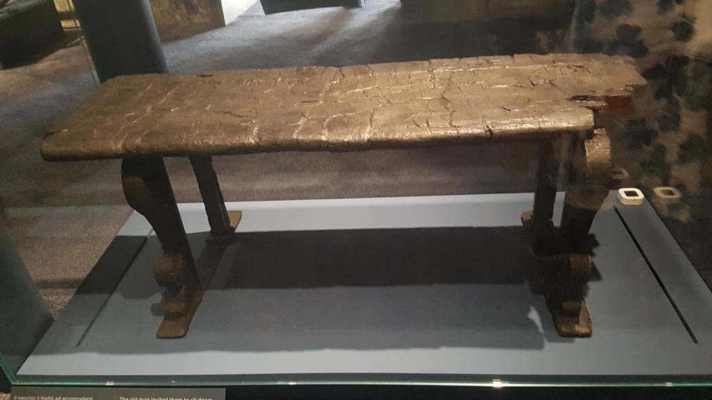 Decumanus Maximus, Herculaneum. August 2023.
Carbonised wooden bench/long seat with moulded front legs. Photo courtesy of Maribel Velasco.
On display in exhibition entitled – “Materia. Il legno che non bruciò ad Ercolano”.